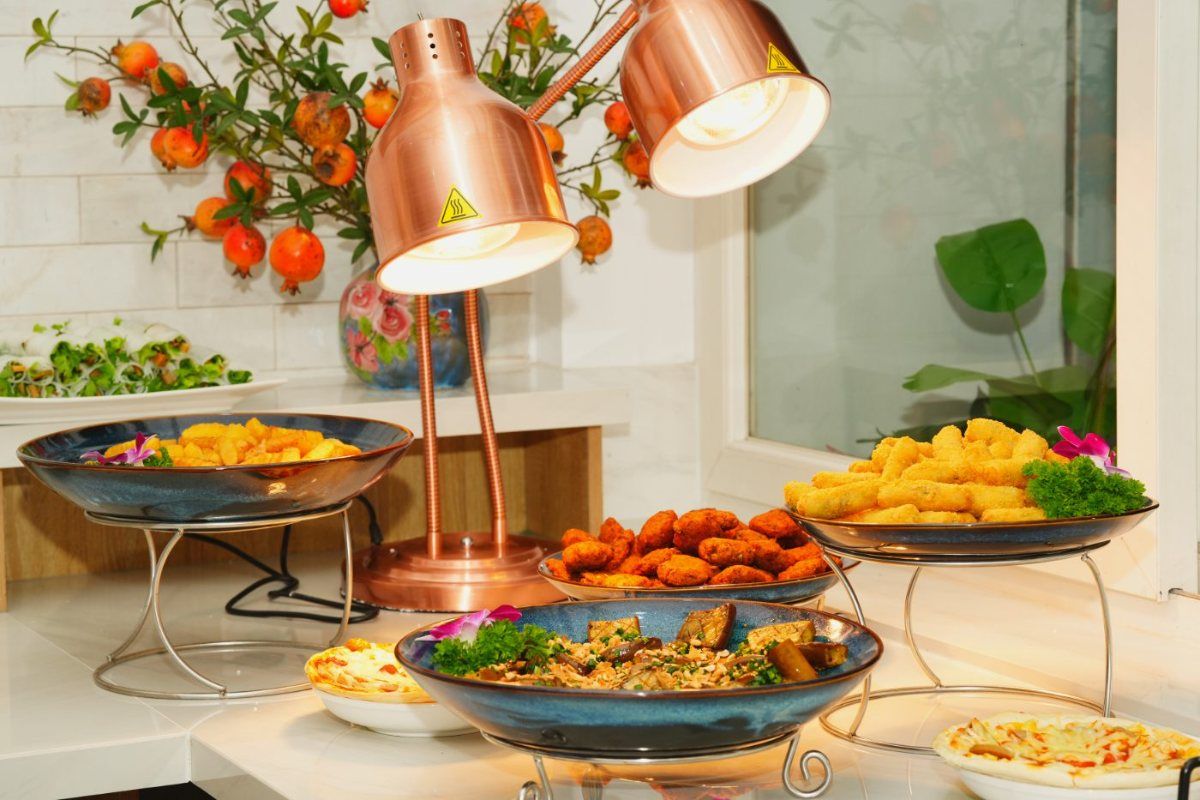 Quầy buffet chay Mộc Lâm ngày rằm — khay món dưới đèn giữ nhiệt